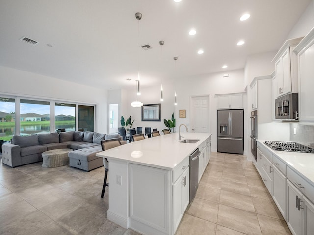 kitchen with a breakfast bar area, stainless steel appliances, a kitchen island with sink, white cabinets, and sink