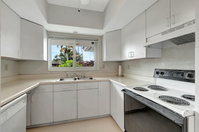 kitchen with white appliances, white cabinets, sink, light tile patterned floors, and a tray ceiling