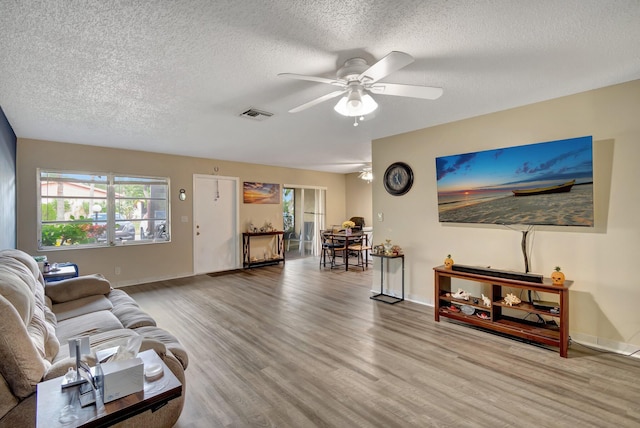 living room featuring a wealth of natural light, ceiling fan, wood-type flooring, and a textured ceiling