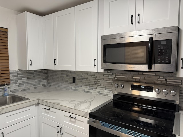 kitchen with appliances with stainless steel finishes, white cabinets, light stone counters, and tasteful backsplash