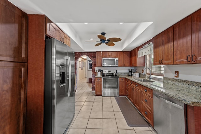 kitchen with sink, light tile patterned floors, a tray ceiling, light stone counters, and stainless steel appliances