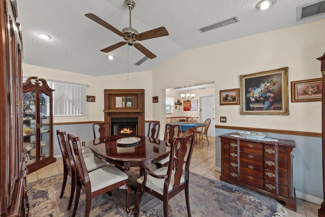 tiled dining space featuring a textured ceiling, vaulted ceiling, and ceiling fan with notable chandelier