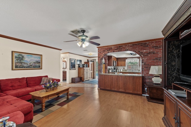 living room featuring a textured ceiling, crown molding, light hardwood / wood-style floors, and brick wall