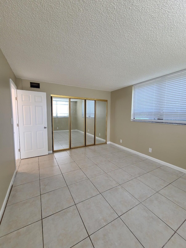 unfurnished bedroom featuring a textured ceiling, a closet, and light tile patterned flooring