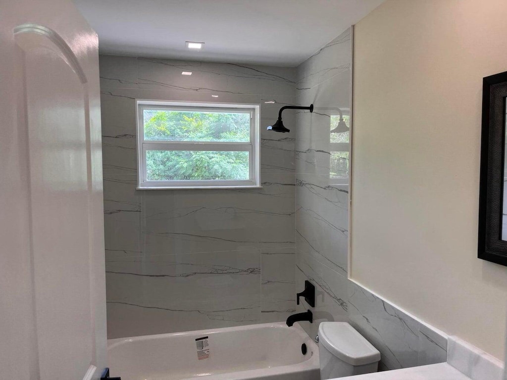 bathroom featuring tiled shower / bath, toilet, and tile walls