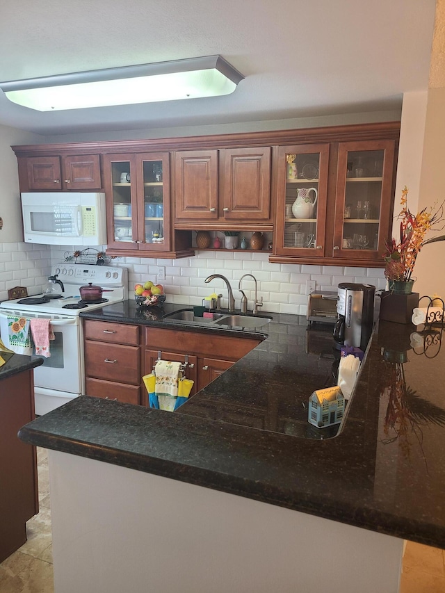 kitchen with white appliances, a peninsula, a sink, glass insert cabinets, and backsplash