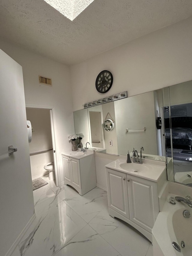 bathroom with a washtub, vanity, a textured ceiling, and toilet