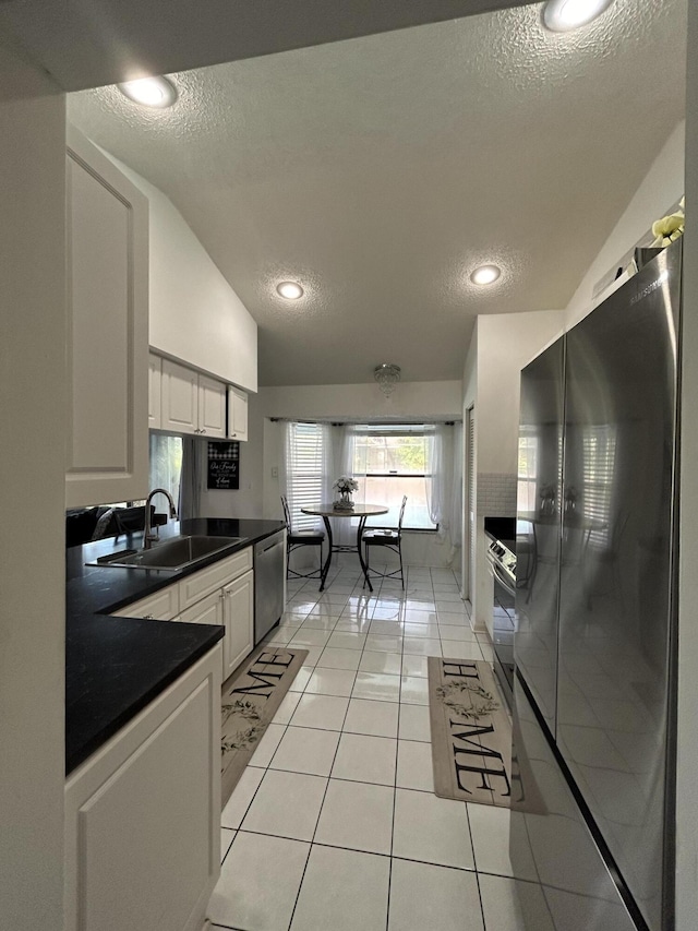 kitchen featuring lofted ceiling, white cabinets, refrigerator, sink, and a textured ceiling