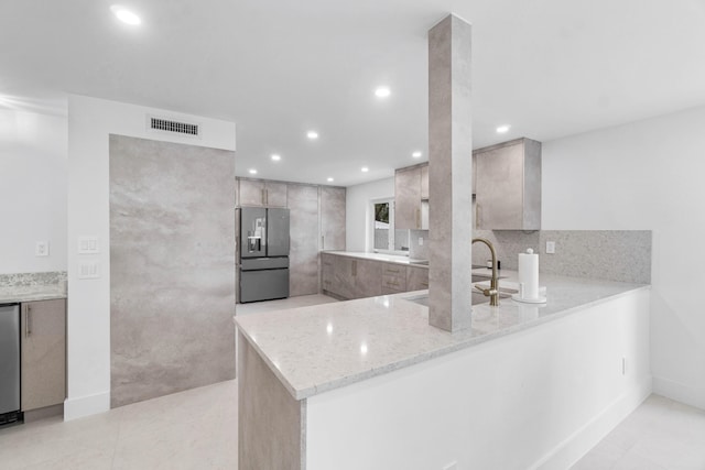 kitchen featuring light stone countertops, stainless steel refrigerator with ice dispenser, kitchen peninsula, sink, and light brown cabinets