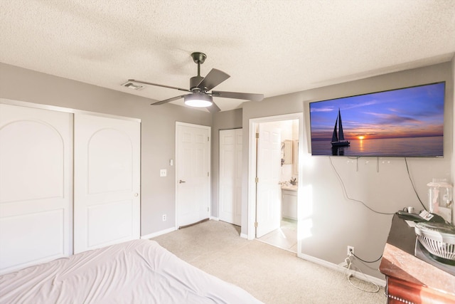 unfurnished bedroom with ceiling fan, ensuite bathroom, light carpet, and a textured ceiling