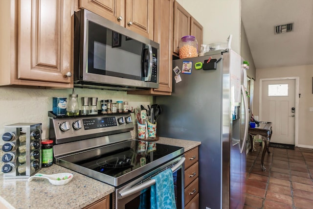 kitchen with dark tile patterned flooring, vaulted ceiling, light stone counters, and appliances with stainless steel finishes