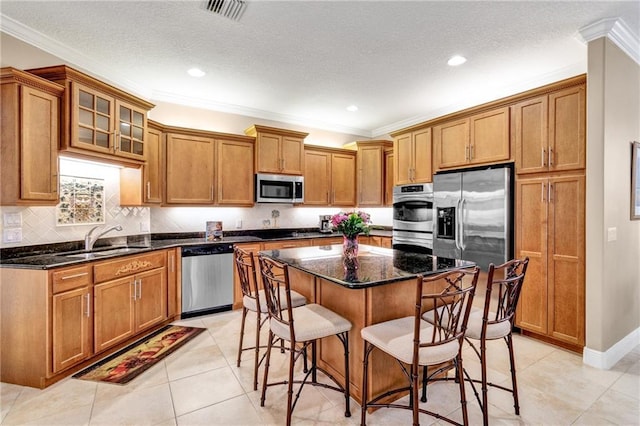 kitchen featuring crown molding, dark stone counters, a breakfast bar area, a kitchen island, and appliances with stainless steel finishes