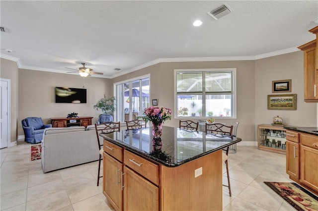 kitchen featuring a kitchen breakfast bar, ornamental molding, ceiling fan, light tile patterned floors, and a center island