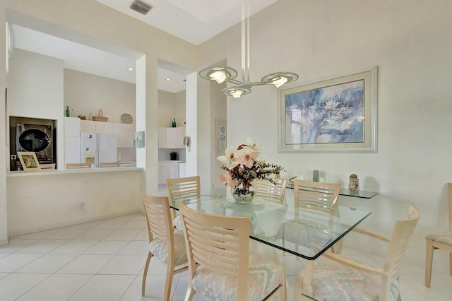 tiled dining space featuring stacked washer and dryer, a towering ceiling, and a chandelier