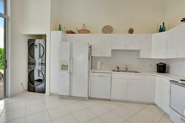 kitchen featuring white cabinets, stacked washing maching and dryer, white appliances, and sink