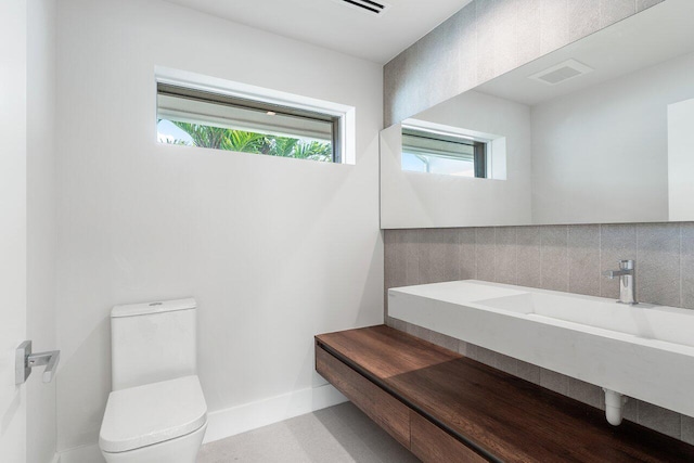 bathroom with a healthy amount of sunlight, sink, tasteful backsplash, and toilet