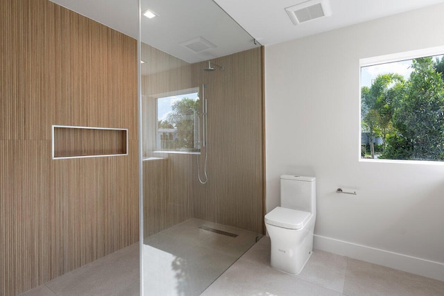 bathroom featuring toilet, a tile shower, and tile patterned floors