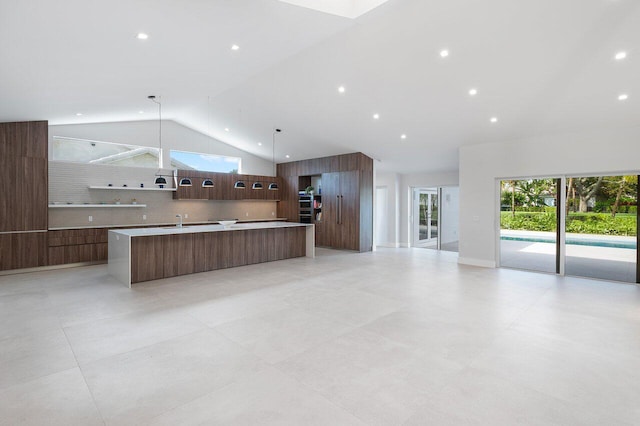 kitchen with an island with sink, decorative light fixtures, high vaulted ceiling, and tasteful backsplash