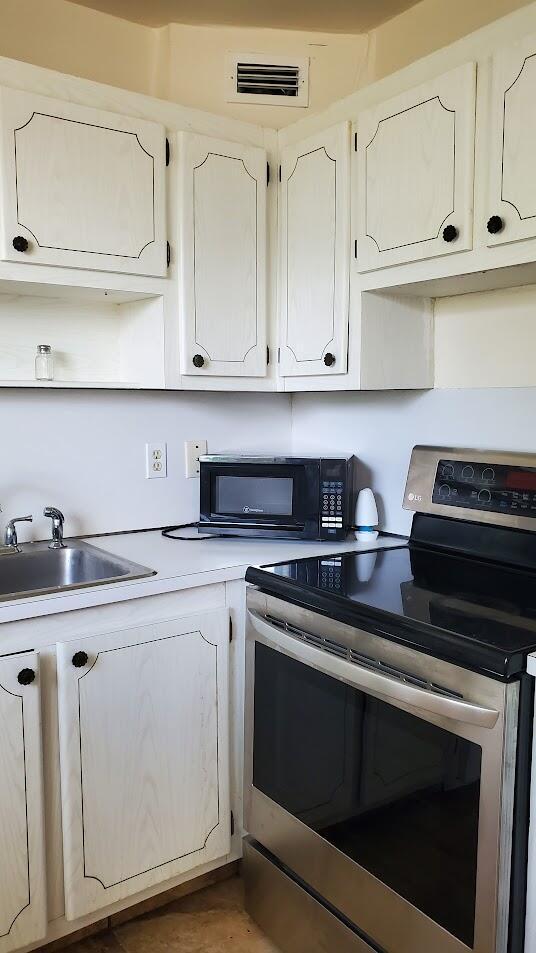 kitchen with black microwave, visible vents, white cabinets, stainless steel range with electric cooktop, and light countertops