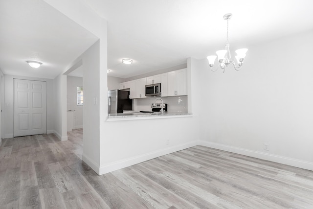 kitchen with an inviting chandelier, white cabinets, hanging light fixtures, appliances with stainless steel finishes, and kitchen peninsula