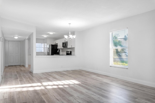 unfurnished living room featuring a chandelier, light wood-type flooring, plenty of natural light, and sink