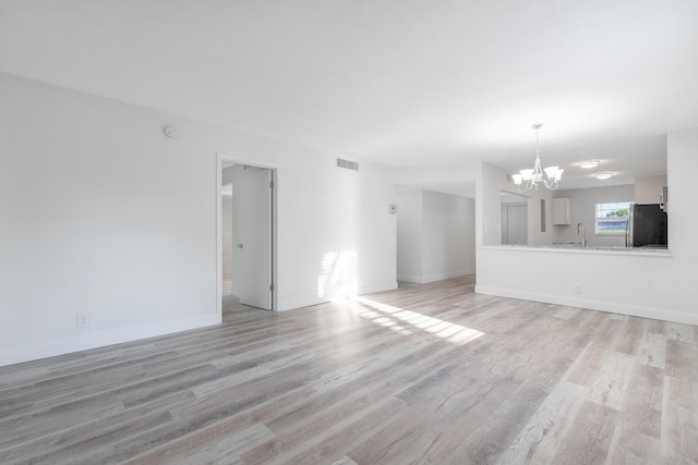 unfurnished living room featuring a notable chandelier, sink, and light hardwood / wood-style flooring