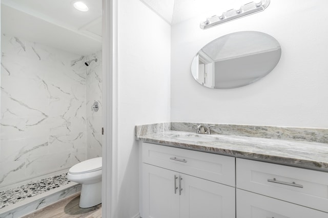 bathroom featuring hardwood / wood-style floors, vanity, toilet, and tiled shower