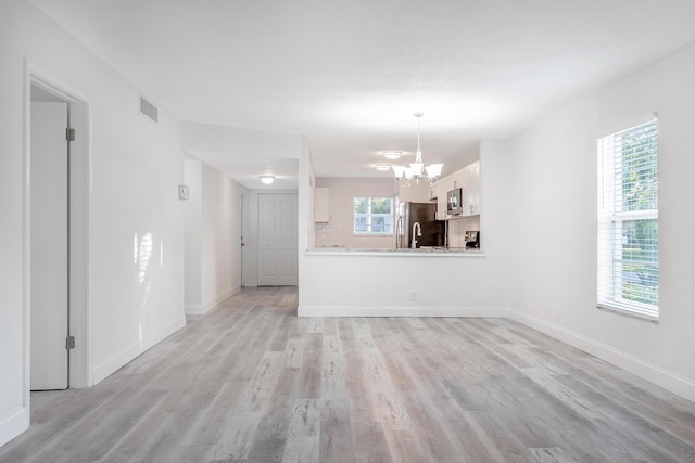 unfurnished living room featuring light wood-type flooring and an inviting chandelier