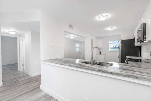 kitchen with light stone countertops, light wood-type flooring, stainless steel appliances, sink, and white cabinets