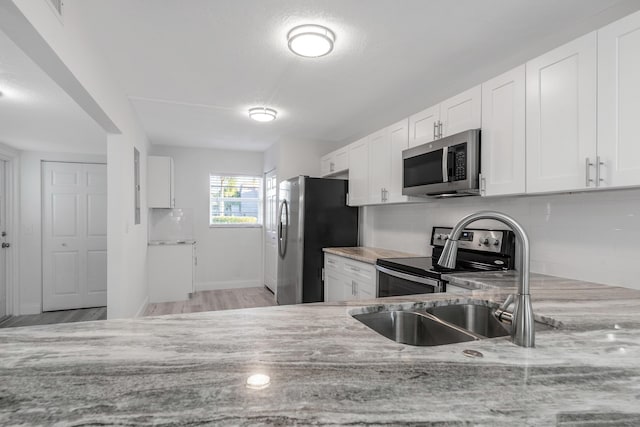 kitchen with backsplash, white cabinets, light hardwood / wood-style flooring, light stone countertops, and appliances with stainless steel finishes