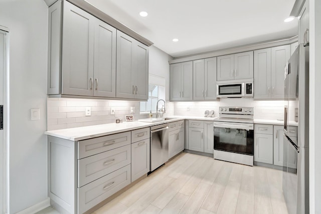 kitchen with decorative backsplash, light wood-type flooring, stainless steel appliances, sink, and gray cabinets