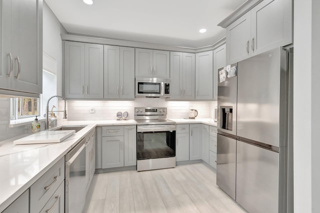 kitchen featuring gray cabinetry, sink, appliances with stainless steel finishes, tasteful backsplash, and light hardwood / wood-style floors