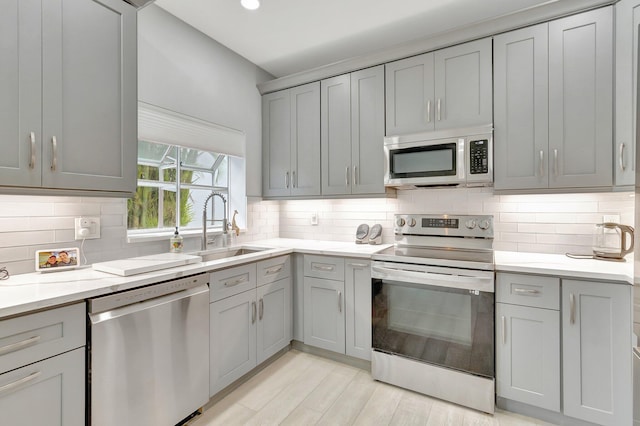 kitchen with appliances with stainless steel finishes, tasteful backsplash, light stone counters, sink, and gray cabinets