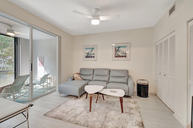 living room featuring ceiling fan, a textured ceiling, and light hardwood / wood-style flooring