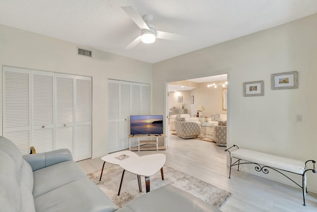 living room featuring ceiling fan with notable chandelier, light hardwood / wood-style floors, and a textured ceiling