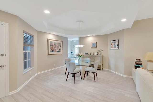 dining room with a tray ceiling and light hardwood / wood-style flooring