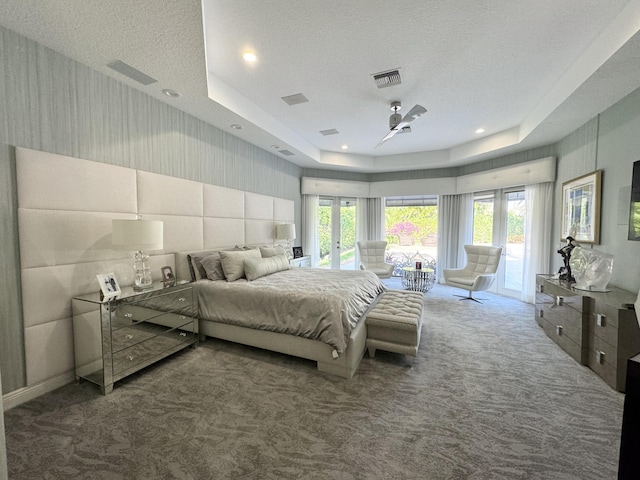 carpeted bedroom featuring a textured ceiling, access to outside, multiple windows, and a tray ceiling