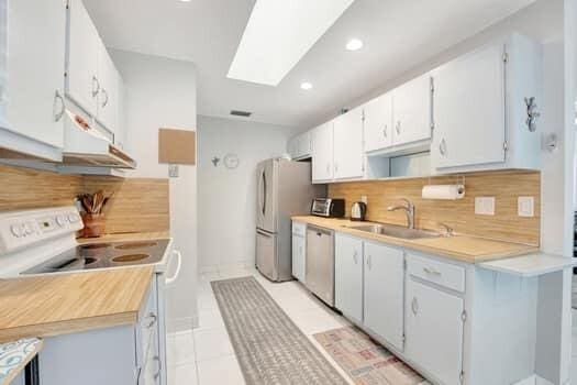 kitchen with white cabinets, sink, a skylight, decorative backsplash, and stainless steel appliances