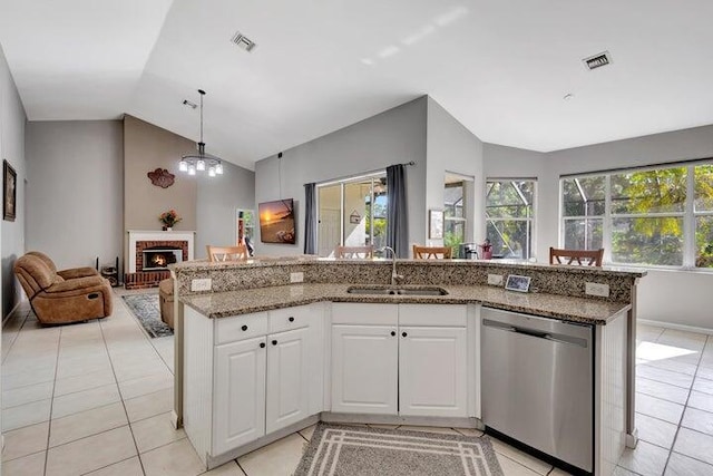 kitchen with lofted ceiling, sink, a brick fireplace, stainless steel dishwasher, and white cabinetry