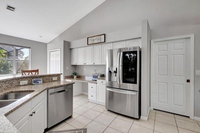 kitchen featuring light stone countertops, white cabinetry, stainless steel appliances, lofted ceiling, and light tile patterned floors