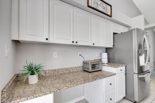 kitchen with light stone countertops, stainless steel refrigerator with ice dispenser, light tile patterned floors, and white cabinetry