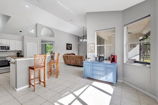 kitchen featuring a breakfast bar, an inviting chandelier, white cabinets, vaulted ceiling, and stainless steel range oven