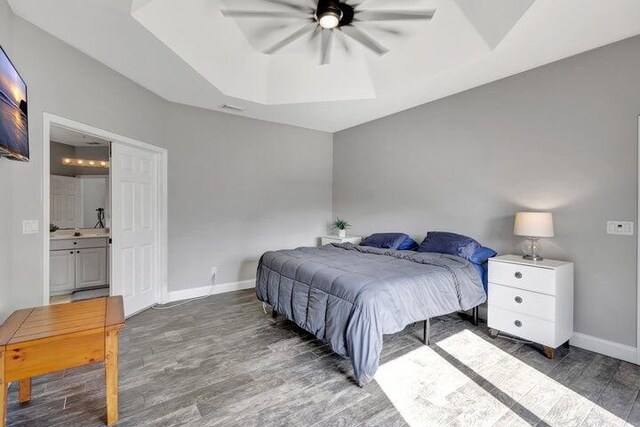 bedroom with a raised ceiling, connected bathroom, ceiling fan, and dark hardwood / wood-style flooring