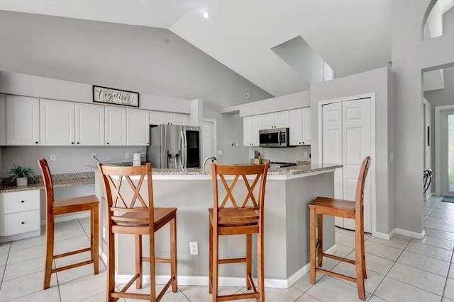 kitchen with a breakfast bar, light tile patterned floors, an island with sink, appliances with stainless steel finishes, and white cabinetry