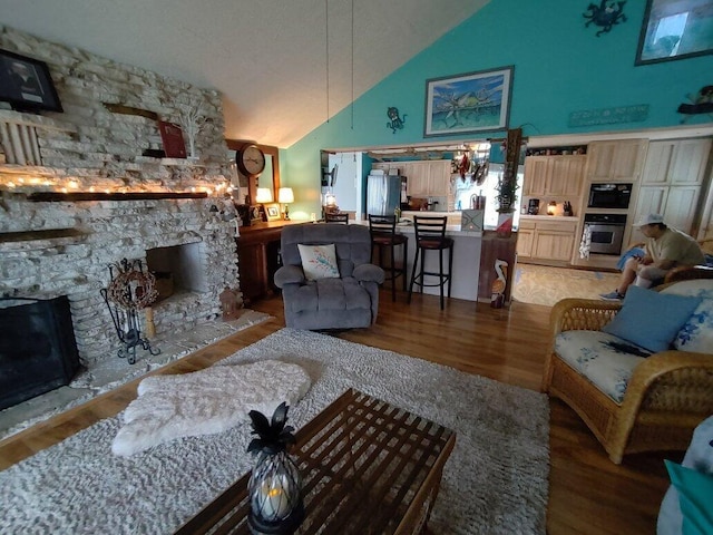 living room with lofted ceiling, a stone fireplace, and hardwood / wood-style floors