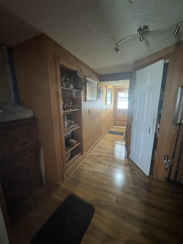 hallway with built in features, wood walls, a textured ceiling, and hardwood / wood-style floors