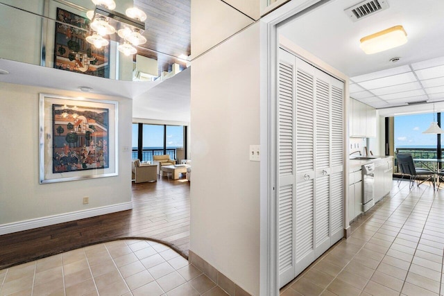 corridor featuring a notable chandelier, light tile patterned flooring, sink, and floor to ceiling windows