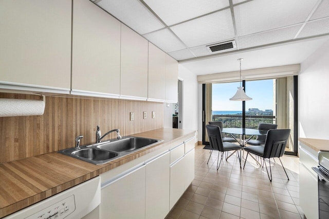 kitchen featuring a drop ceiling, sink, white cabinets, hanging light fixtures, and butcher block counters