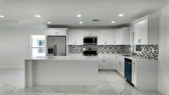 kitchen with decorative backsplash, appliances with stainless steel finishes, a kitchen island, sink, and white cabinetry