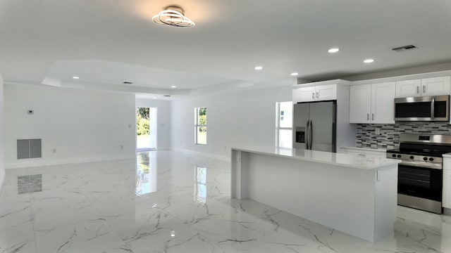 kitchen featuring white cabinets, appliances with stainless steel finishes, a raised ceiling, and a kitchen island